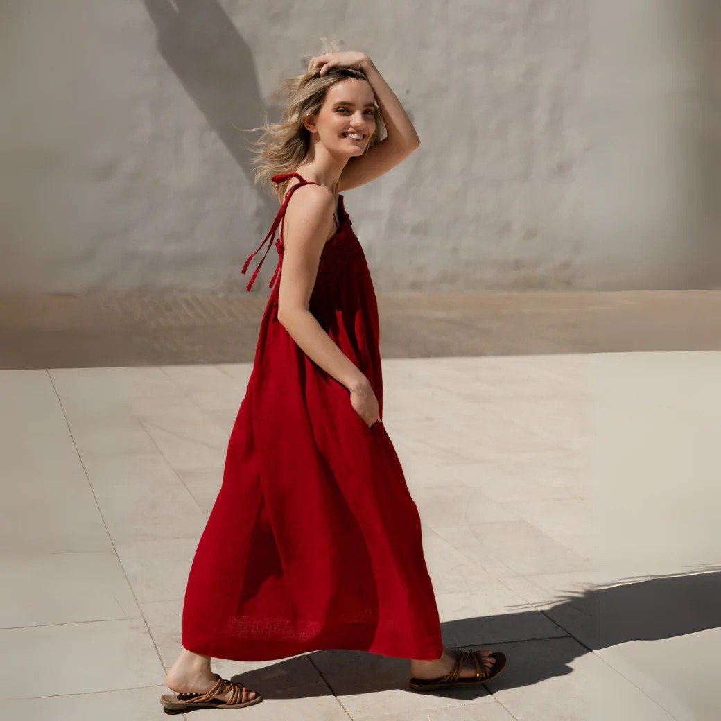 1. Woman wearing red linen Ballade dress with tie straps walking outdoors on sunny day