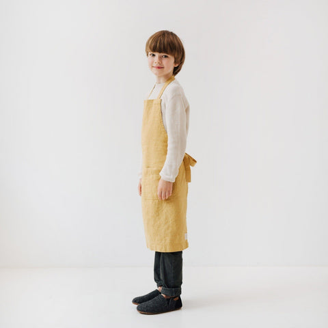 5. Side view of child in honey-colored linen apron standing in a bright, minimalist setting
