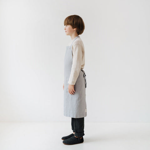 4. Side profile of child in light grey linen apron in a bright setting
