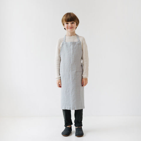 1. Child wearing light grey linen apron standing in a bright room