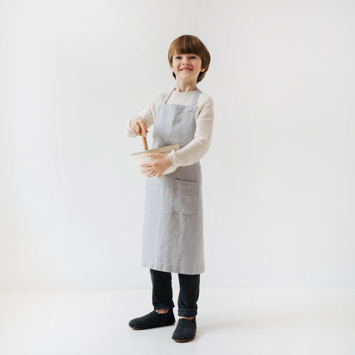 6. Child stirring bowl while wearing light grey linen apron