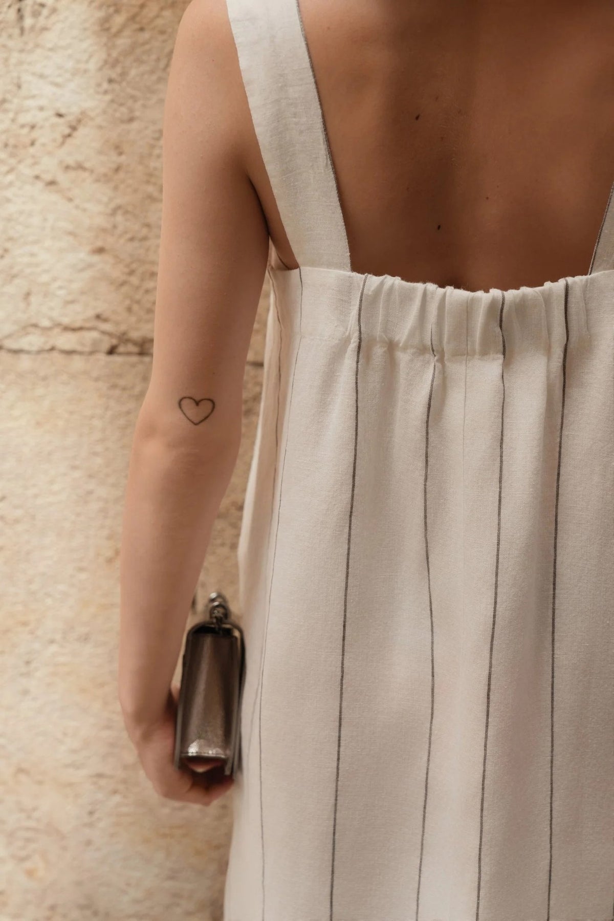 3. Close-up of back of milk white linen dress with grey stripes showing elasticated detail and heart tattoo