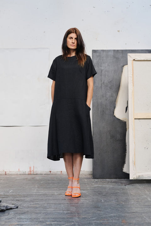 1. Woman in black linen dress with orange heels standing in art studio, front view