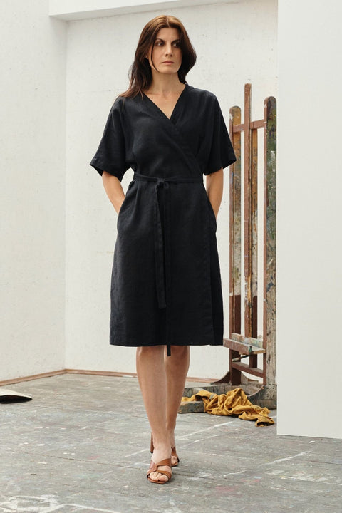 1. Woman wearing black linen wrap dress with V-neck and tied fastening, standing in an art studio setting