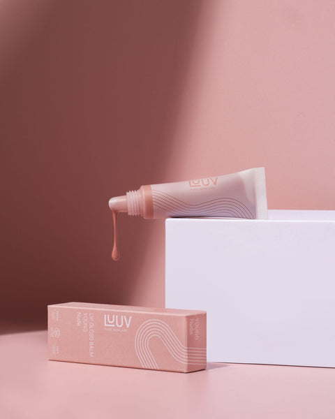 1. LUUV Lip Gloss Balm in tube with packaging, shown in a lifestyle setting with soft pink background