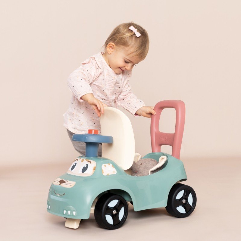 1. Toddler opening seat storage of Smoby Little Ride-on Pusher in pastel colors, indoor setting