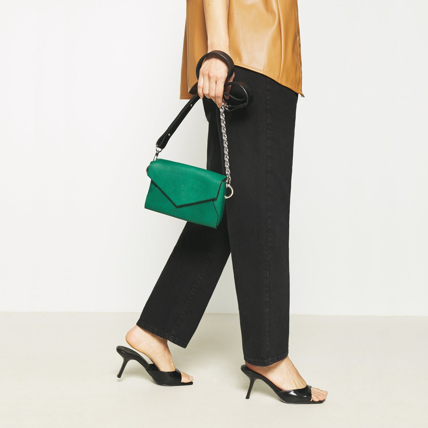 1. Woman carrying Daz Studio green leather envelope bag with black strap and chain detail, styled with black pants and heels
