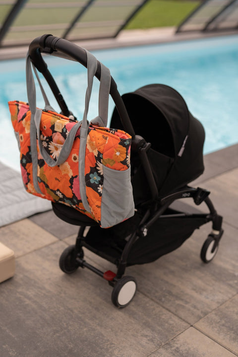 1. Floral weekender bag with blue straps attached to a stroller by a pool, highlighting its practicality for parents.