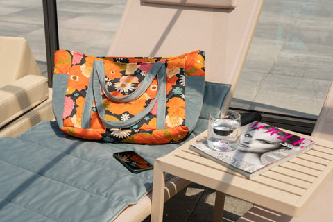 1. Floral weekender bag with blue straps placed on a sun lounger by a pool, next to a magazine and a glass of water.