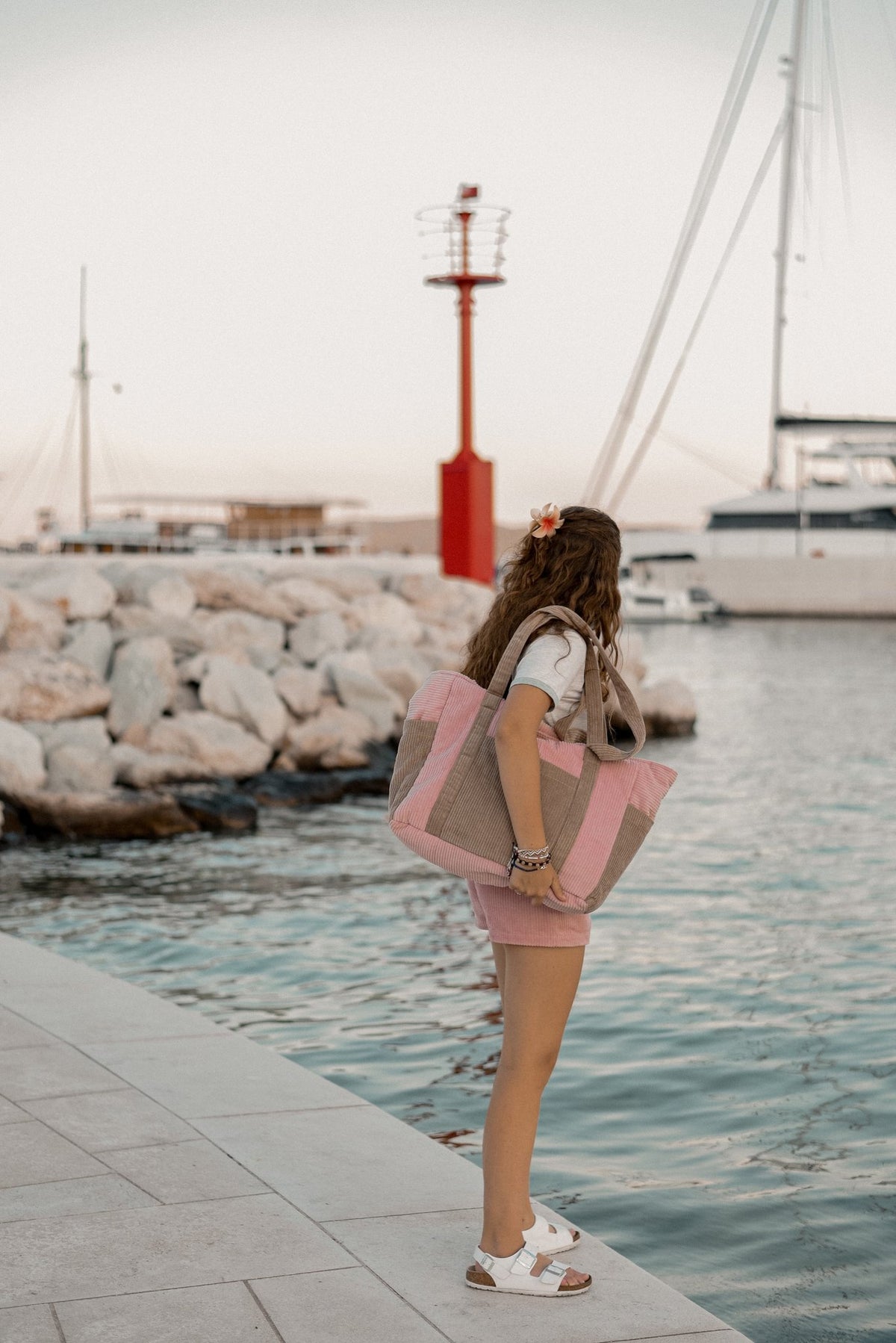6. Woman standing by the marina holding pink and coffee-colored weekender bag, wearing casual summer outfit