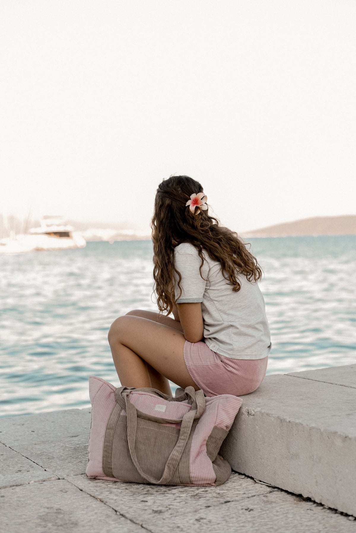 7. Woman sitting on a dock with pink and coffee-colored weekender bag, looking out at the water