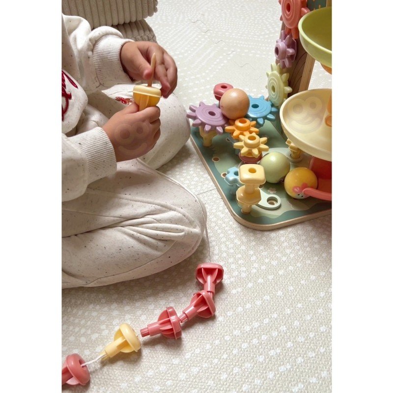 5. Child assembling pieces of the Woopie Montessori 4-in-1 activity tree, focusing on the gear and bead maze components.