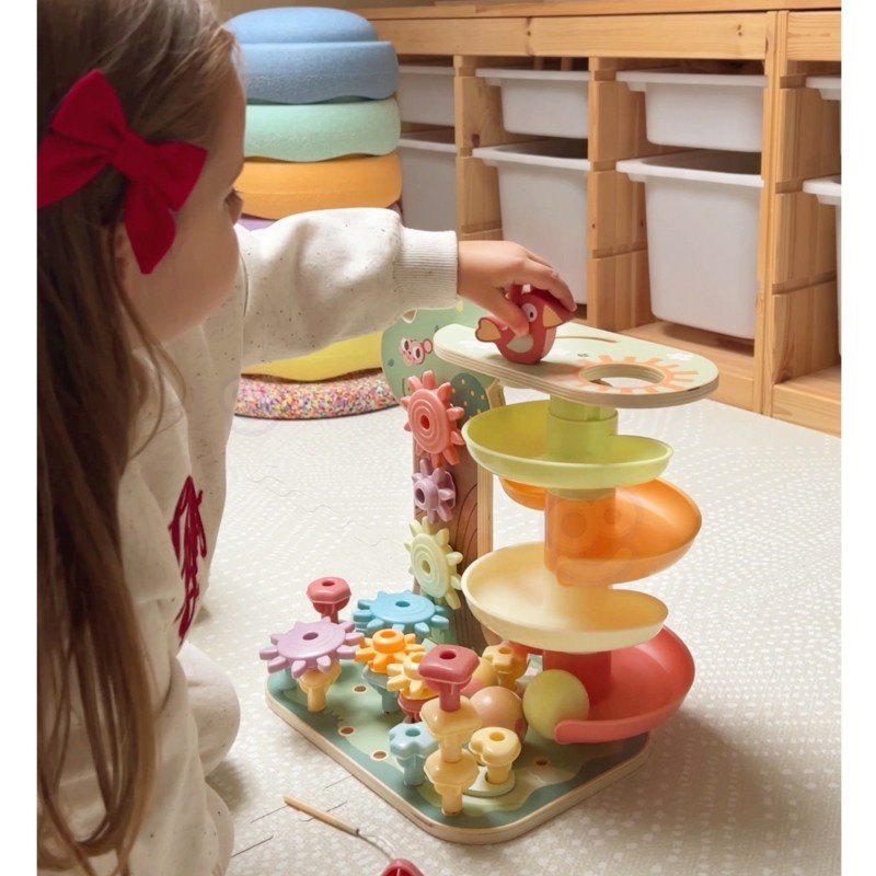 3. Young girl interacting with Woopie Montessori 4-in-1 activity tree, focusing on the marble run feature in a playroom setting.