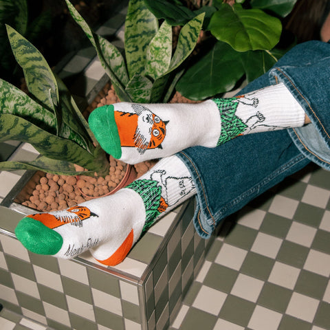 1. Women's Moomin Jungle Retro Socks in white with green and orange accents, worn by a model in a lifestyle setting with plants