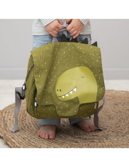 1. Child holding green Mr Dino school bag with dinosaur face and spikes, Trixie Baby
