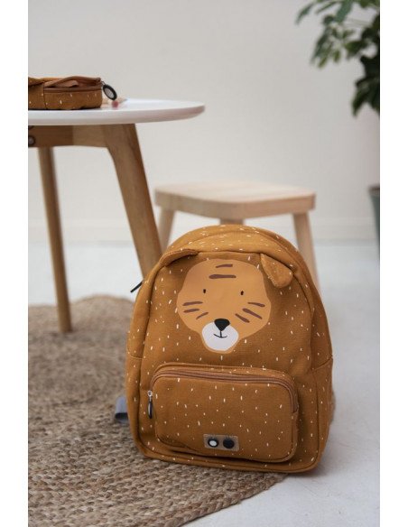 1. Trixie Baby Mr. Tiger backpack placed on a rug next to a table and stool in a cozy room setting