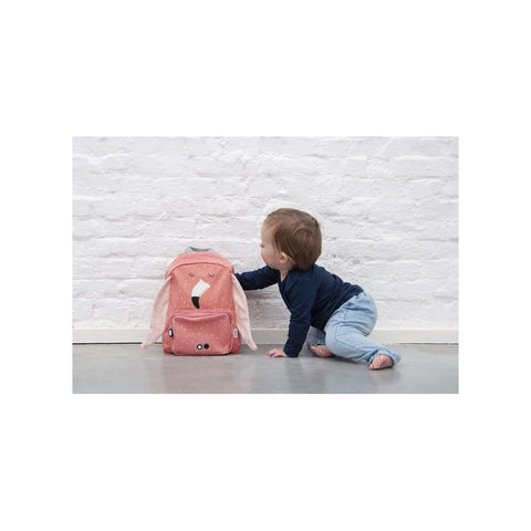 1. Child interacting with pink flamingo-themed backpack on floor, against a white brick wall