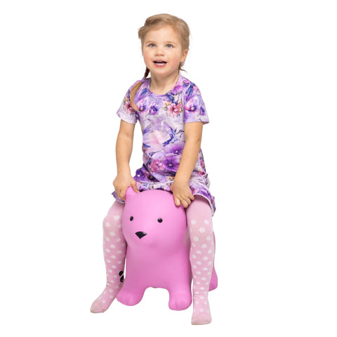 1. Young girl in floral dress and polka dot tights sitting on pink bear-shaped hopper toy smiling in studio setting