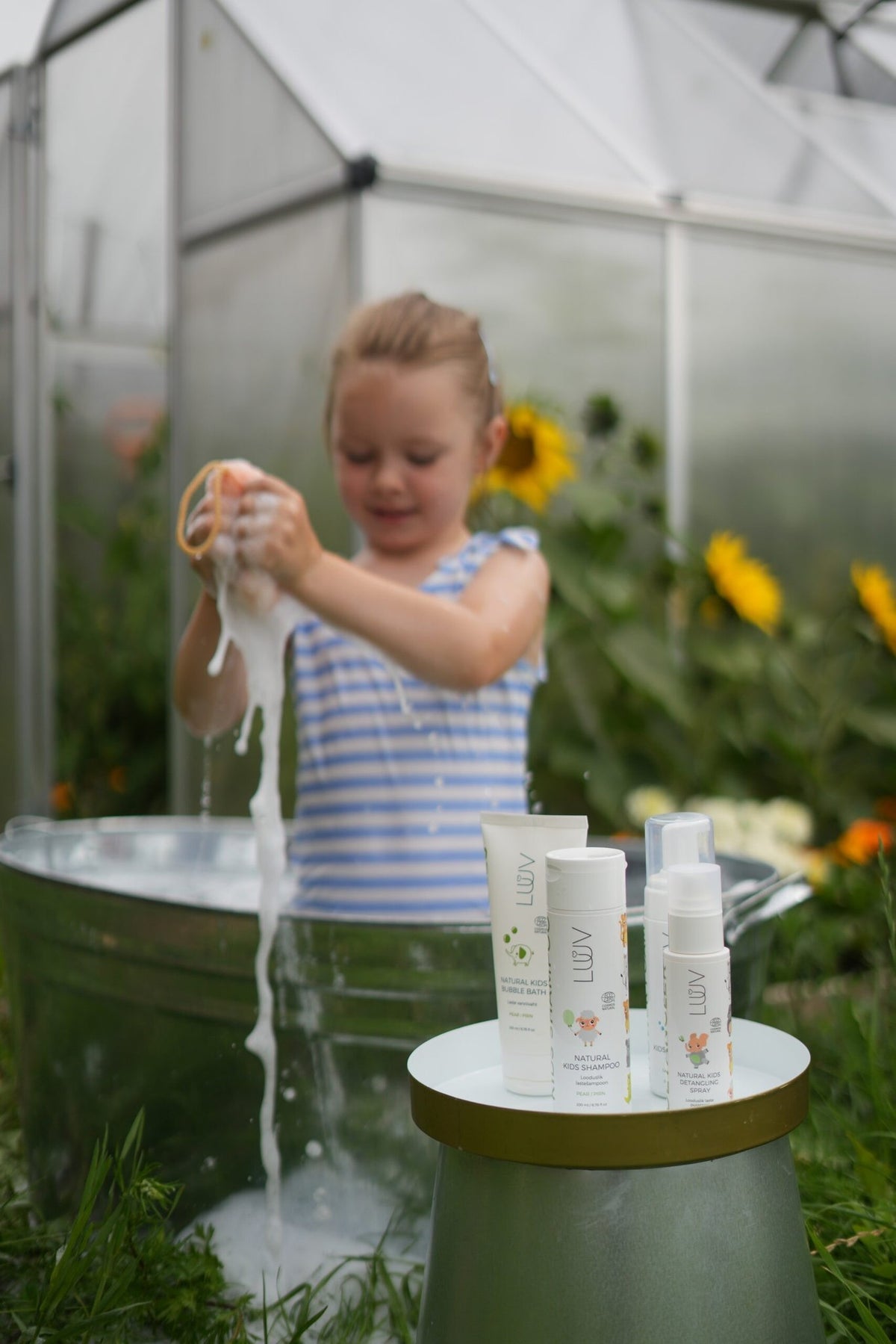 3. Child playing with foam near LUUV Natural Kid's Shampoo Pear COSMOS bottles in garden setting