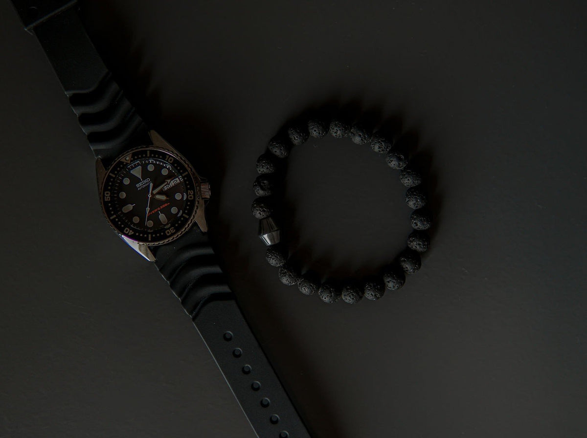 4. Flat lay of Obsidian Lava Stone Bracelet by Canary Lava next to a watch, emphasizing polished lava rocks and Obsidian stone