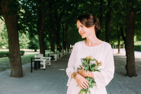 1. Woman in a park wearing Olla's MAAILMAN PARAS ĆITI bracelet in gold, holding flowers