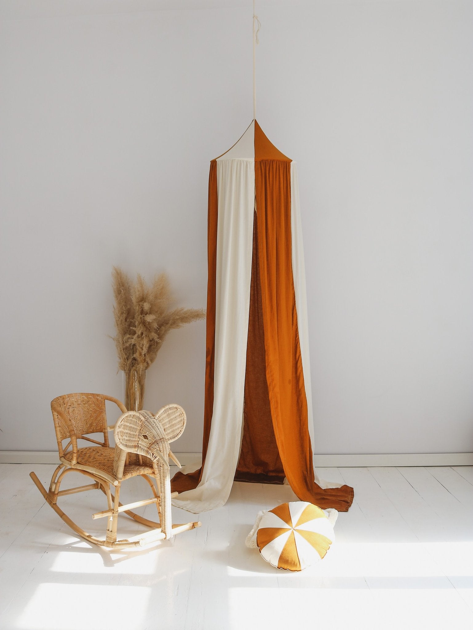 1. Caramel and cream canopy hanging in a bright room with a wicker chair and cushion on the floor