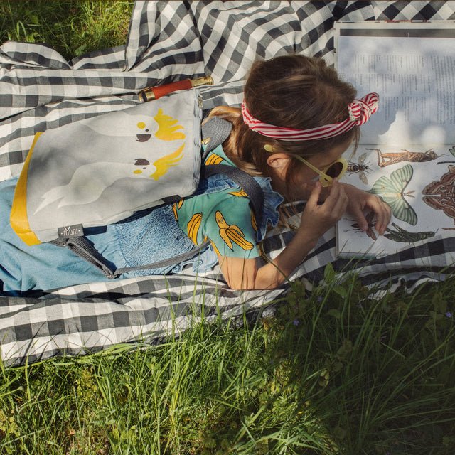 2. Girl lying on grass with Muni Cockatoo kids backpack, highlighting outdoor adventure
