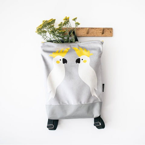 3. Muni Cockatoo backpack in grey velvet with cockatoo design, hanging on a wall with flowers inside