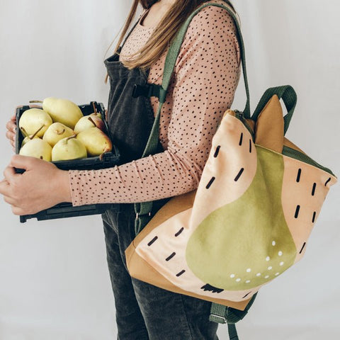 2. Girl holding pears while wearing Muni PEAR backpack, lifestyle setting
