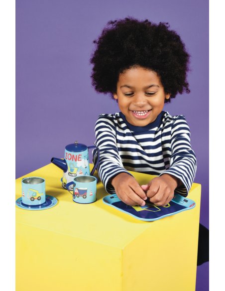 1. Smiling child in striped shirt playing with Floss & Rock construction-themed tea set on yellow table against purple background