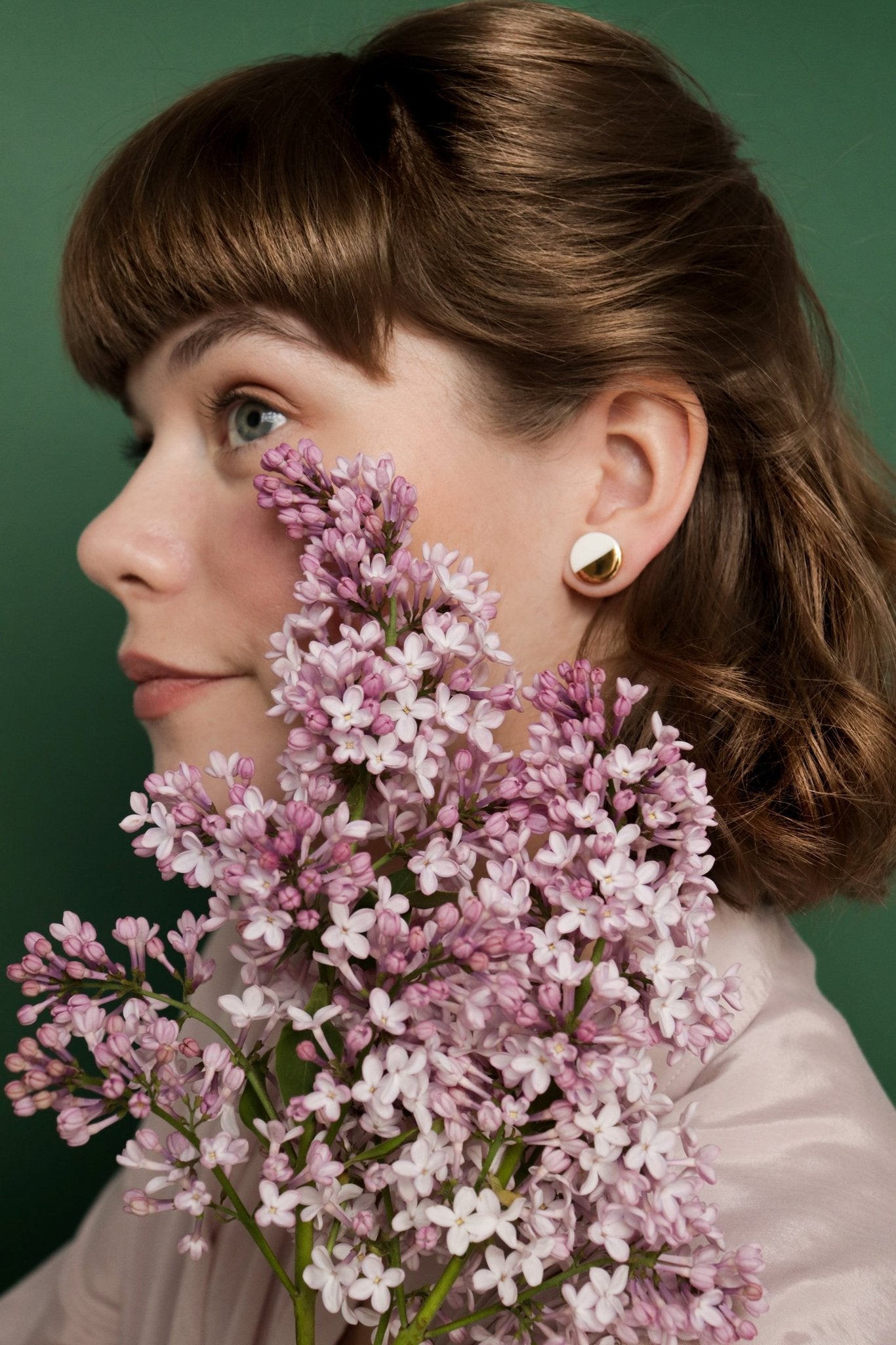 1. Woman wearing Rozenthal Porcelain Round Stud Earrings in green and gold, styled with lilac flowers