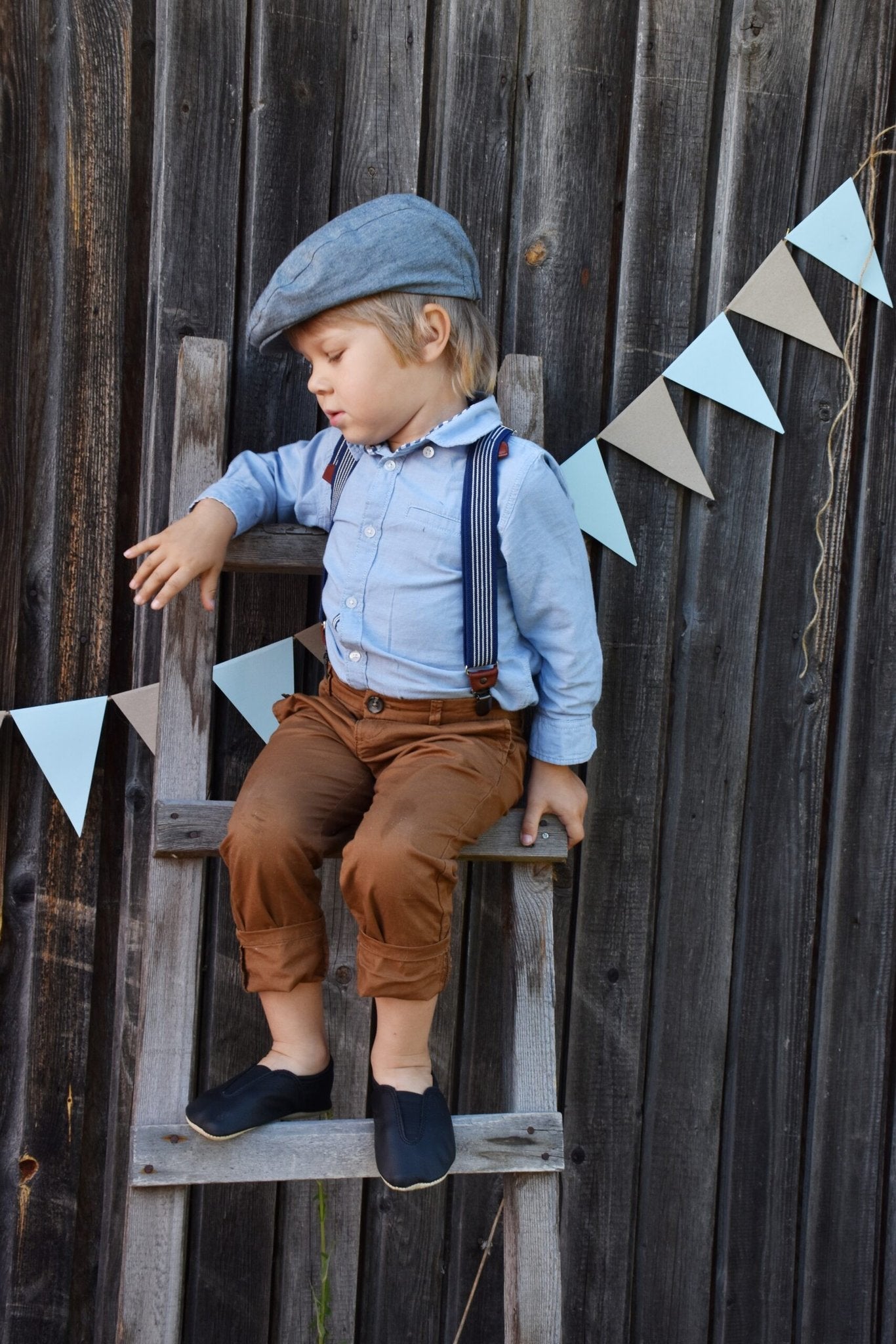 1. Child wearing Hip-Hop Punsa Kids Barefoot Slippers in blue, styled with suspenders and cap, sitting on a wooden ladder outdoors