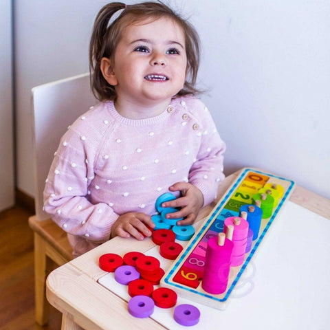 2. Smiling child in pink polka dot sweater playing with colorful wooden counting puzzle at a table