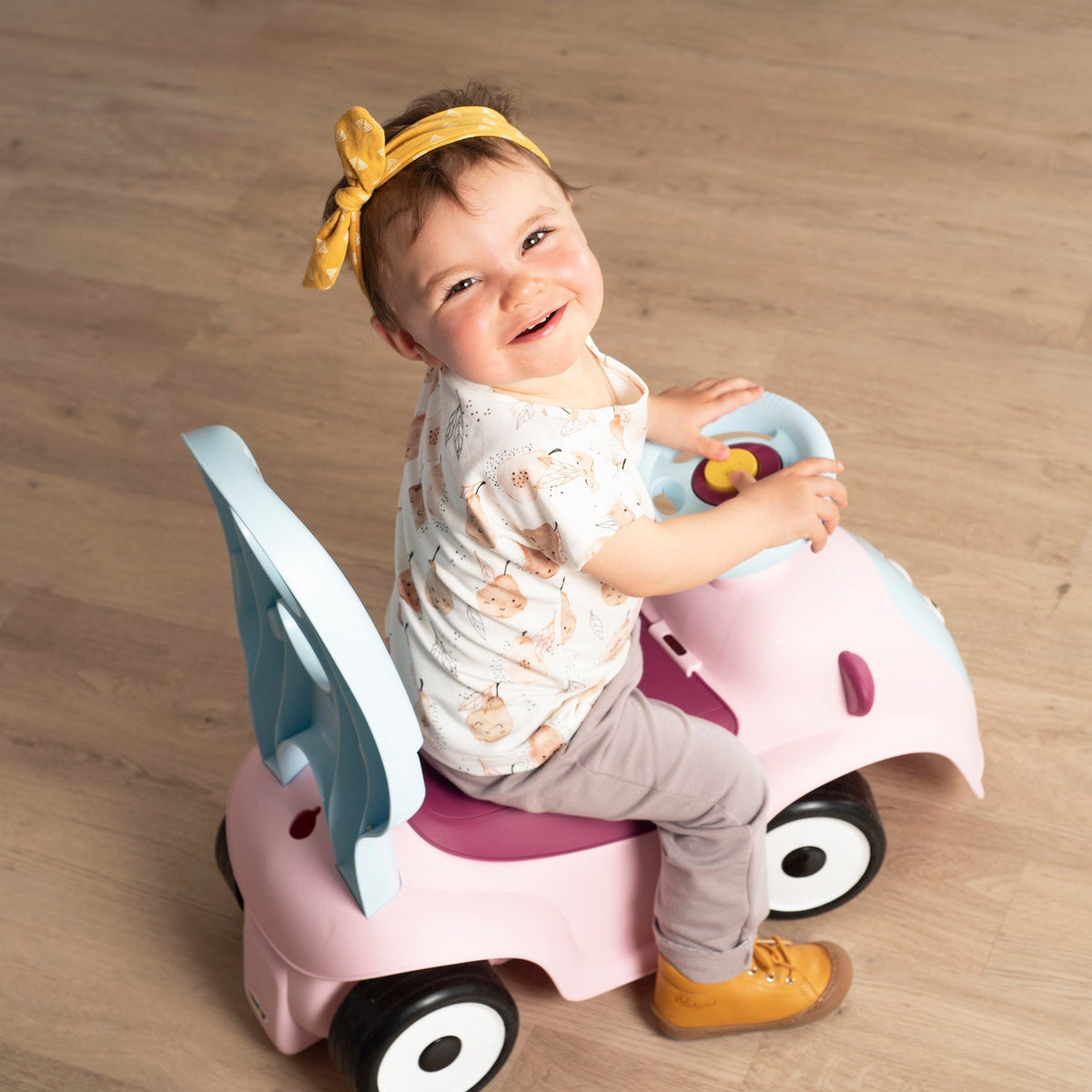 9. Child riding Smoby Ride-on Maestro 3in1 in pink, smiling and looking up, wearing a yellow headband