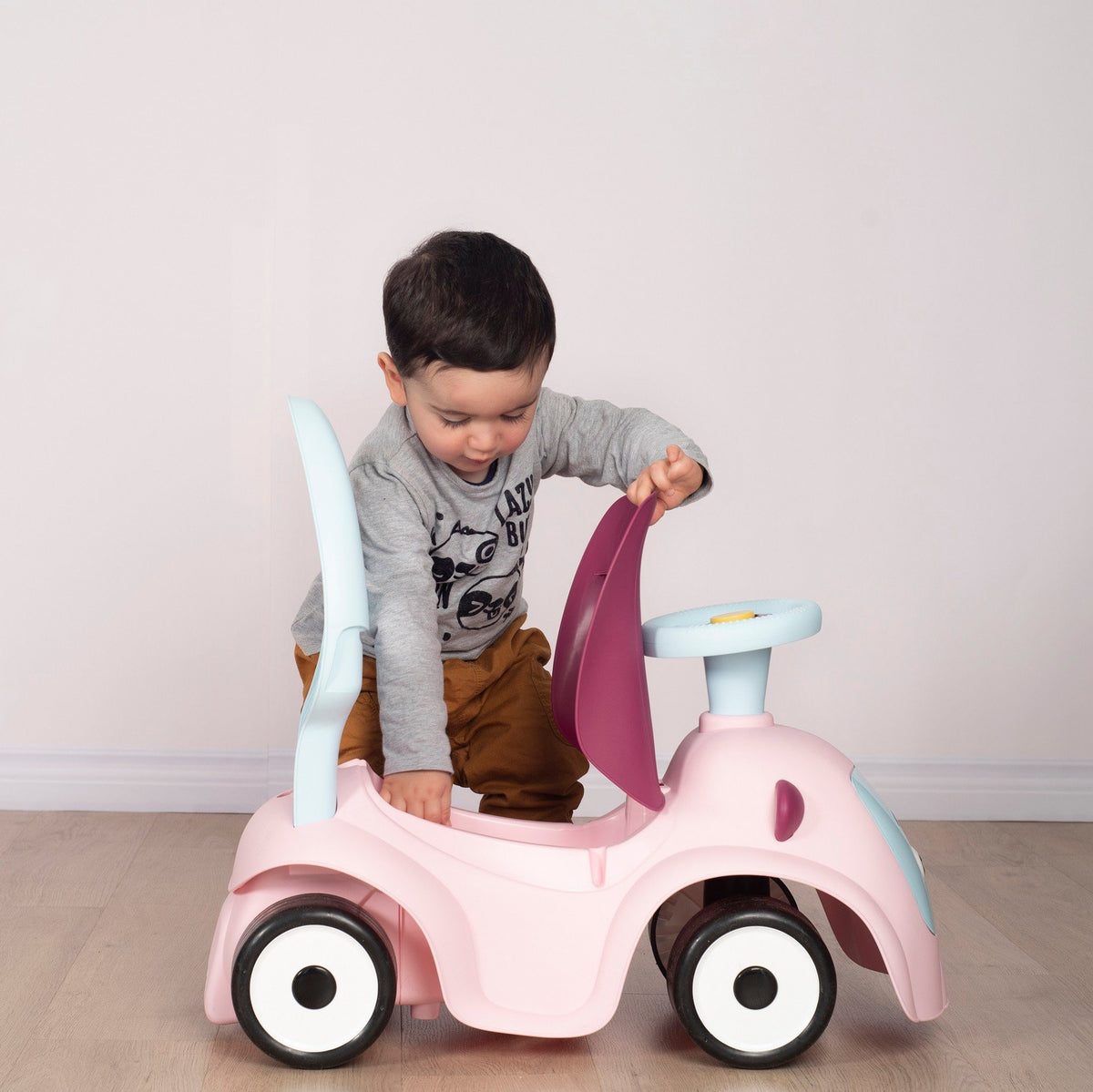 10. Child opening storage compartment of Smoby Ride-on Maestro 3in1 in pink, wearing a grey shirt