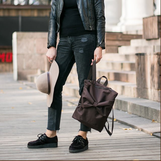 3. Woman holding MUNI brown backpack with bow, standing on wooden steps in urban area