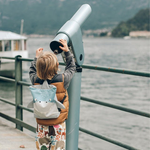 2. Child with Muni shark backpack looking through telescope by the water, highlighting adventure theme
