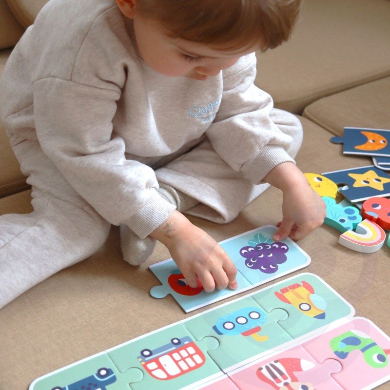 6. Child in grey outfit assembling Woopie Green sensory puzzle on beige couch, focusing on matching shapes