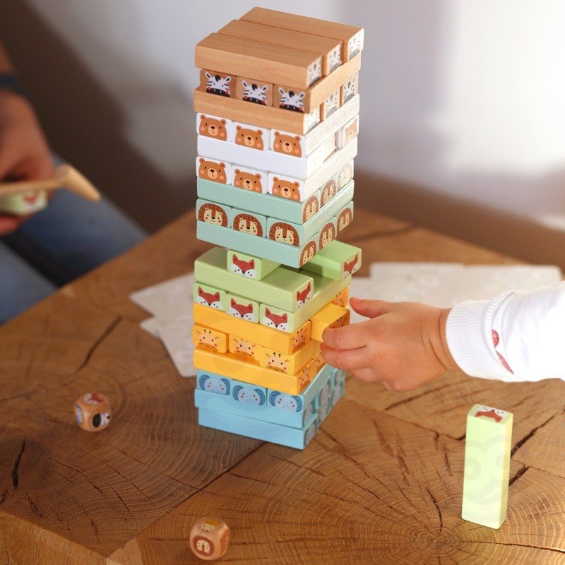 2. Child's hand playing with Shaky Tower game, stacking pastel-colored animal blocks on a wooden table