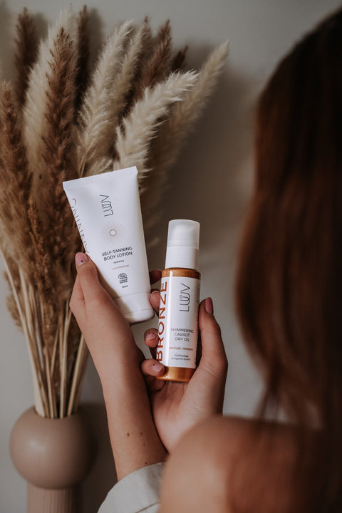 3. LUUV Shimmering Carrot Dry Oil Bronze and self-tanning lotion held by woman, pampas grass background