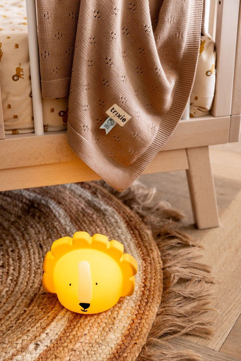 5. Trixie Baby's Mr. Lion silicone night light placed on a woven rug beside a crib in a cozy nursery setting