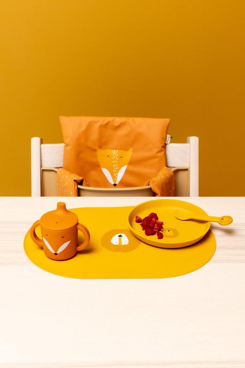 1. Children's dining set with yellow silicone plate, cup, and spoon on table, orange chair cover with fox design in background