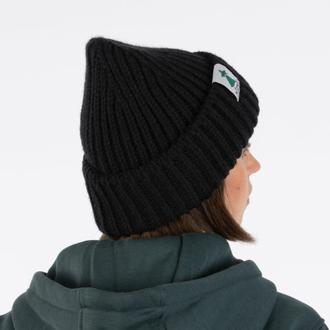 1. Woman wearing black chunky beanie with Moomin by NordicBuddies logo, shown from side, white background