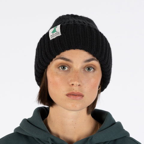 1. Woman wearing black chunky beanie with Moomin by NordicBuddies logo, front view, white background
