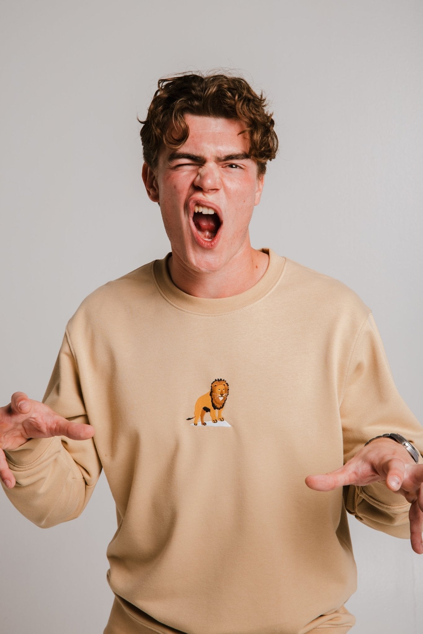 1. Unisex light brown Lion Soft Fleece Sweatshirt by Sossu worn by male model, showcasing playful expression in studio