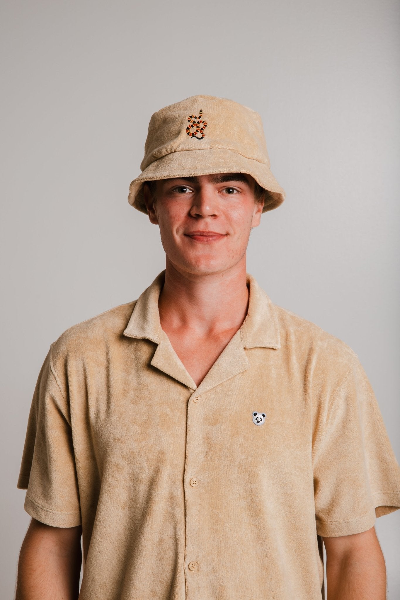 1. Unisex light brown Panda Terry Shirt by Sossu worn by male model with matching bucket hat, studio setting