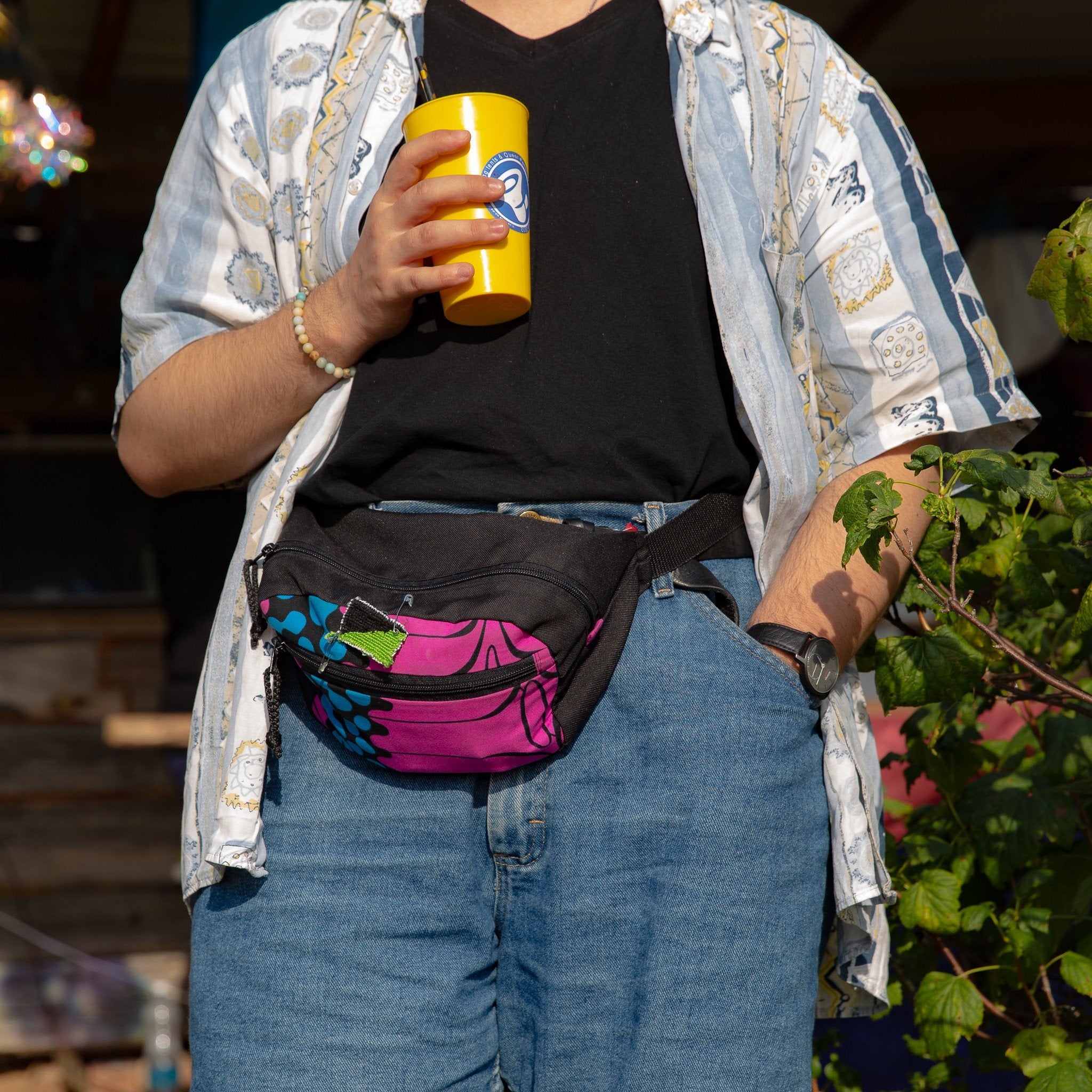 1. Person wearing Drinbags water-resistant waist bag with tropical print at a festival, holding a yellow cup