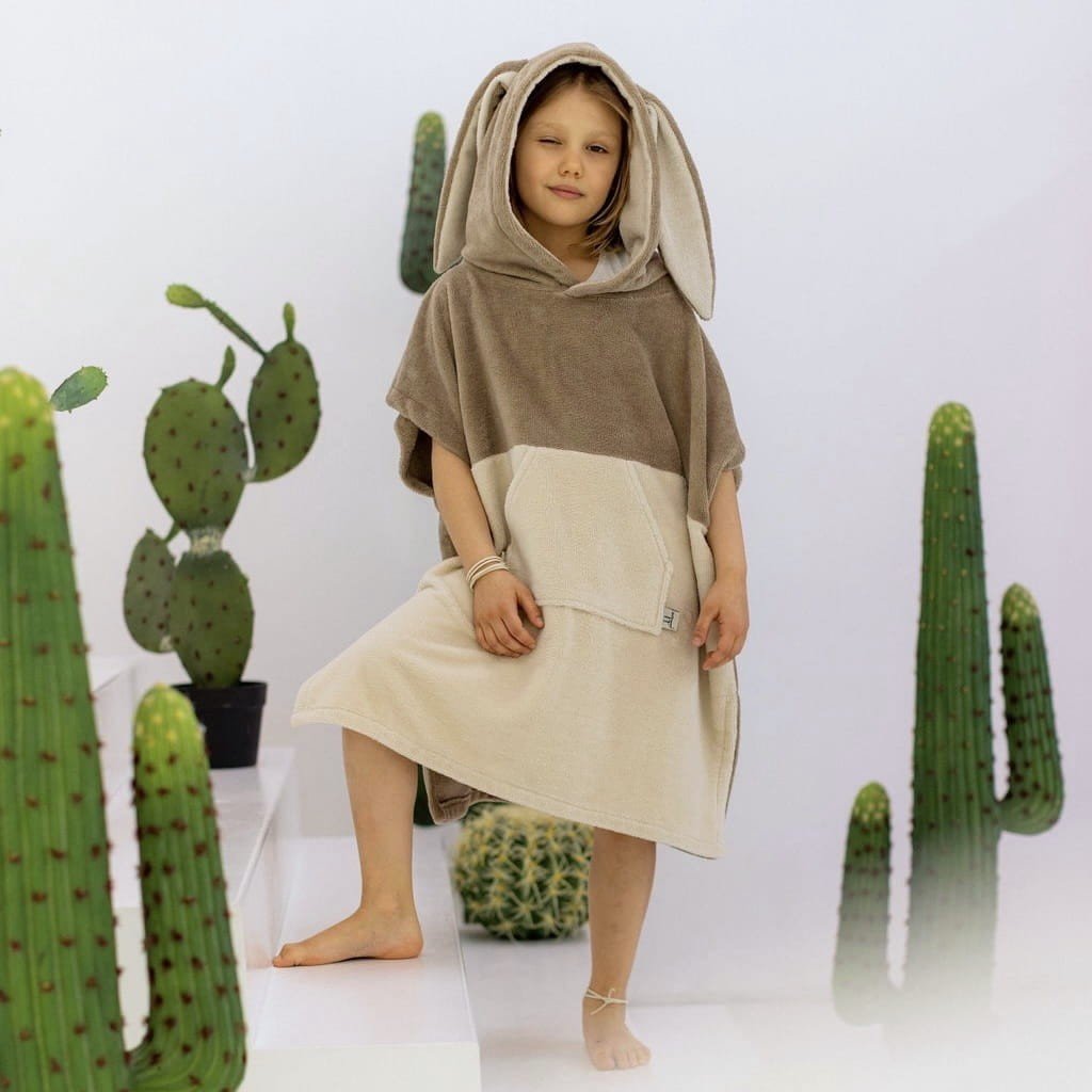 1. Child posing in Patulove Surfbunny kids bath poncho in latte color with hood and kangaroo pocket, surrounded by cacti