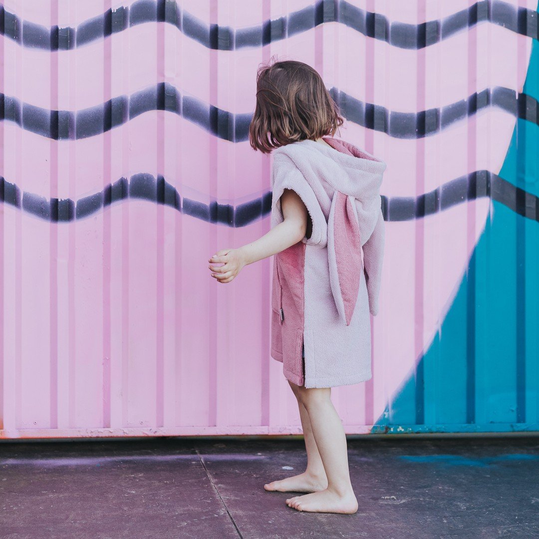 1. Child in pink Surfbunny bath poncho with bunny ears near pink and blue wall