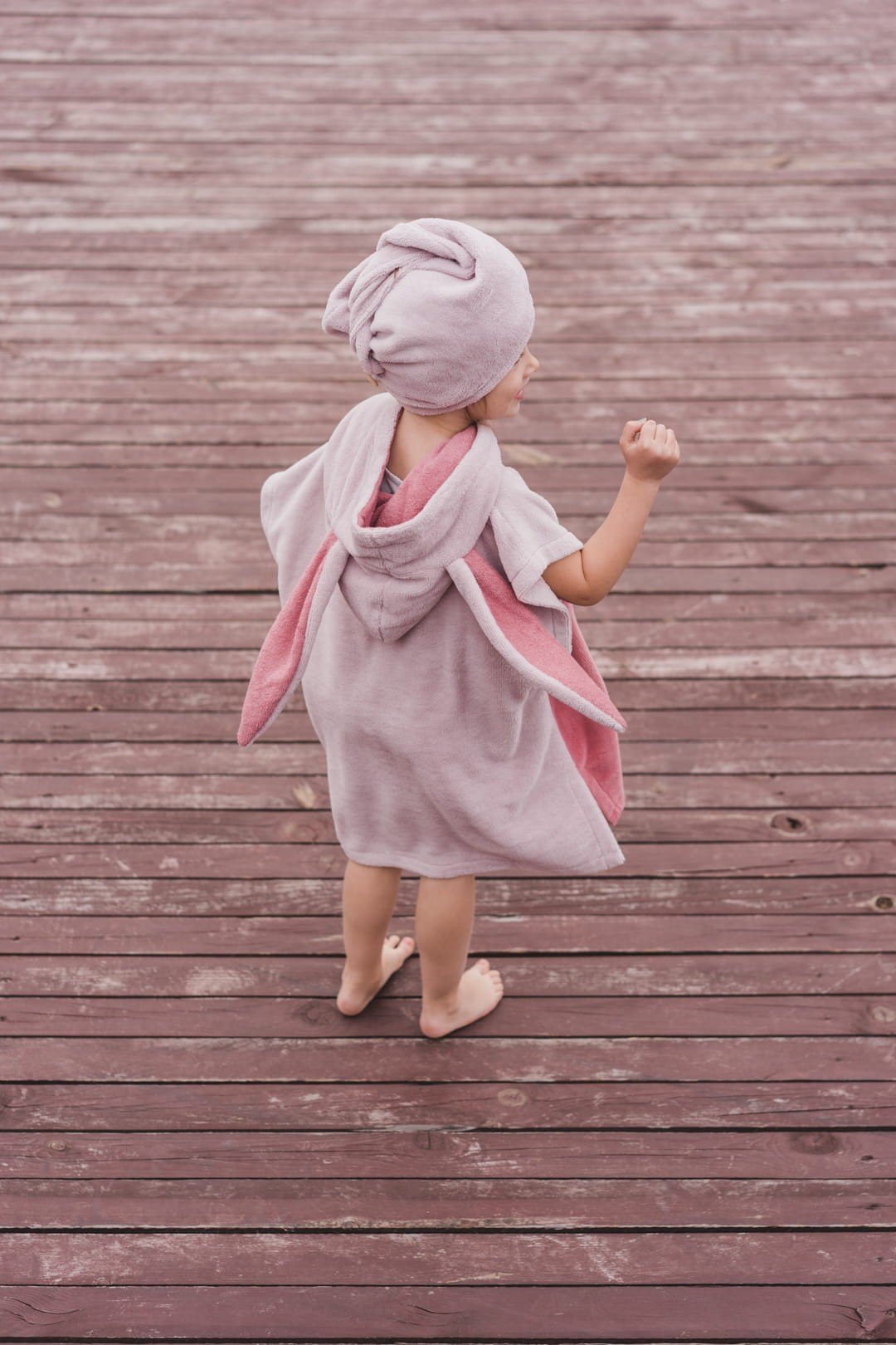 1. Child in pink Surfbunny bath poncho with bunny ears shown from back on wooden deck